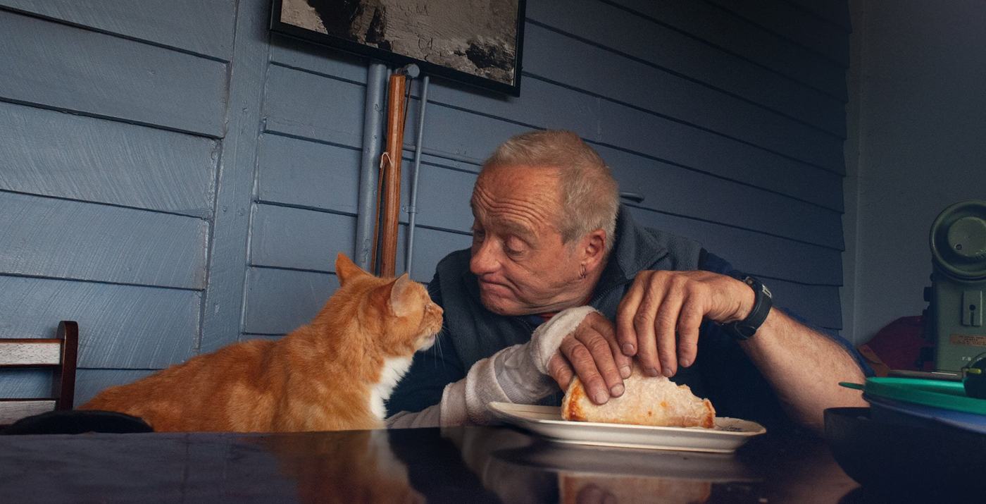 A man sharing a slice of toast with his cat at the kitchen table