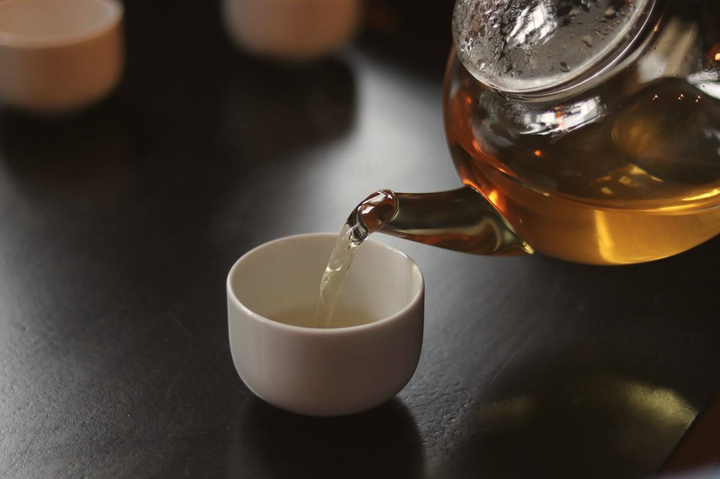 Amber tea poured from a glass teapot into a small white cup