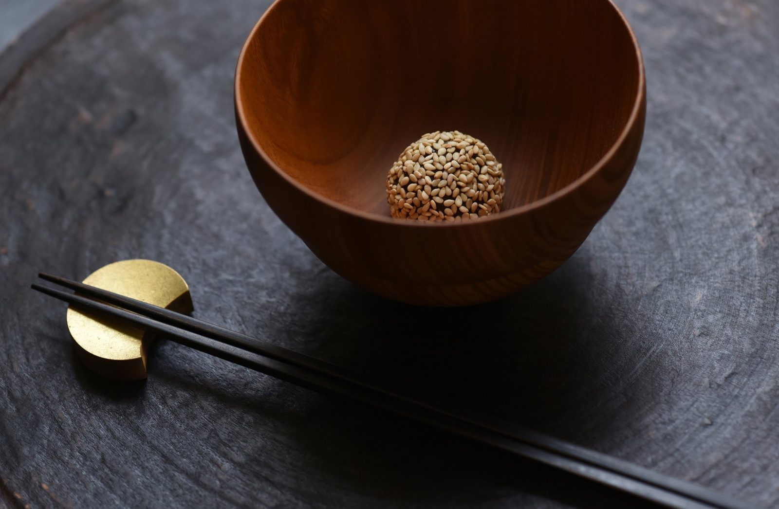 A single sesame miso ball in a wooden bowl, chopsticks on a brass rest