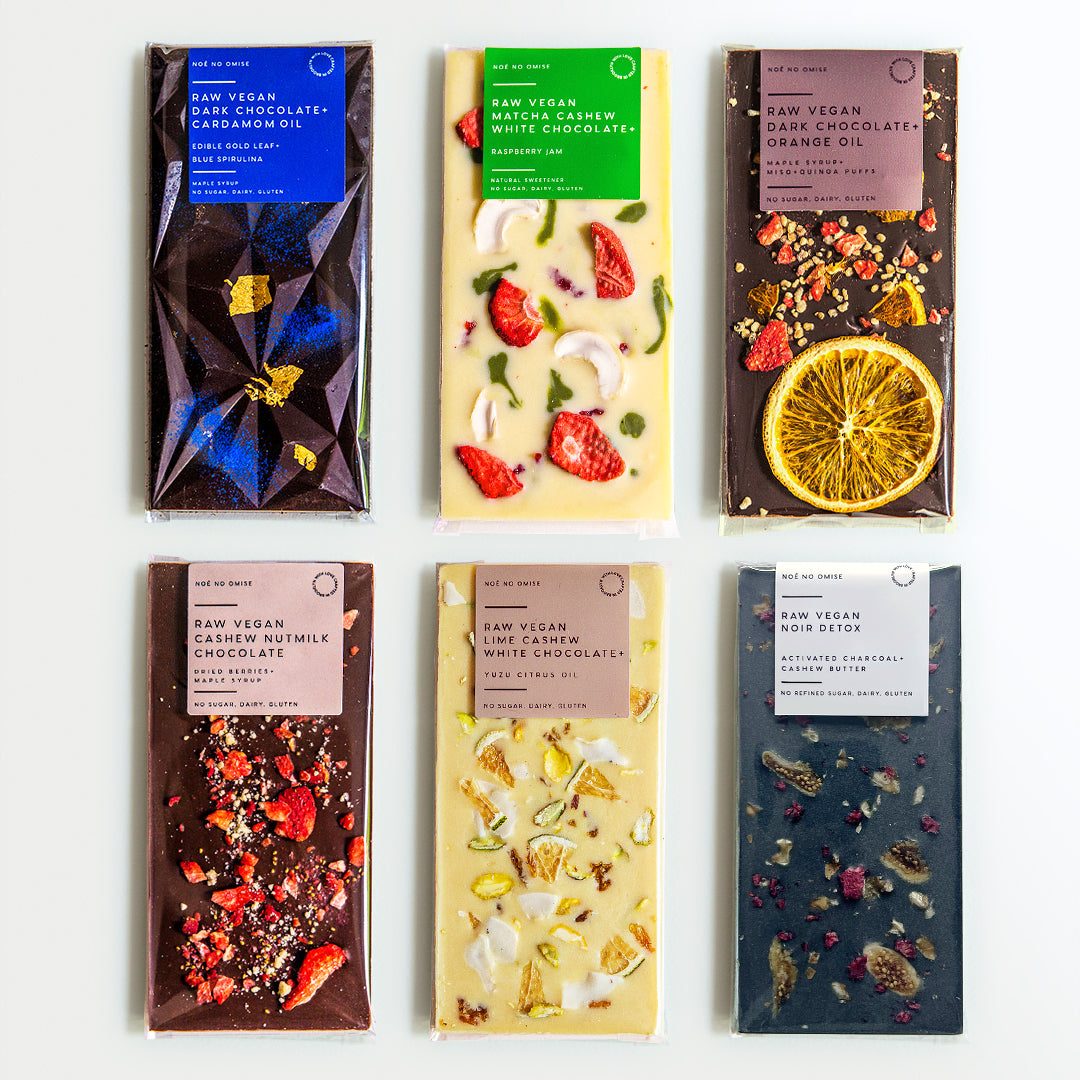 Six NOÉ NO OMISE bars topped with gold leaf, strawberries, orange slices, pistachios and petals