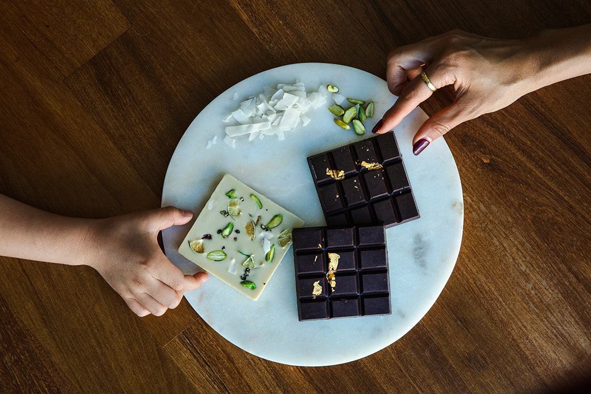 An adult’s and a child’s hands reaching for NOÉ NO OMISE dark and matcha chocolate on a marble board