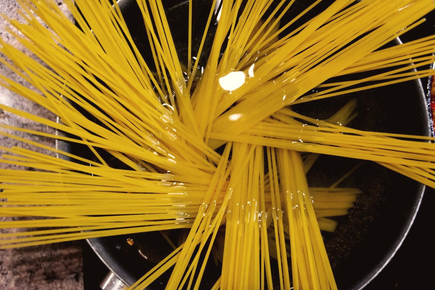 Spaghetti going into a pot of boiling water